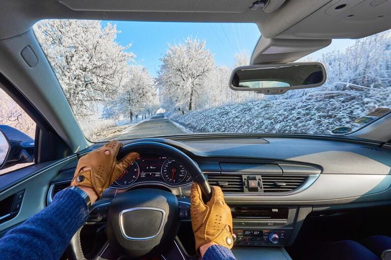 Driver - the first to shoot. Hands on steering wheel in leather gloves in luxury car driving on a winter ice road. Panoramic image.