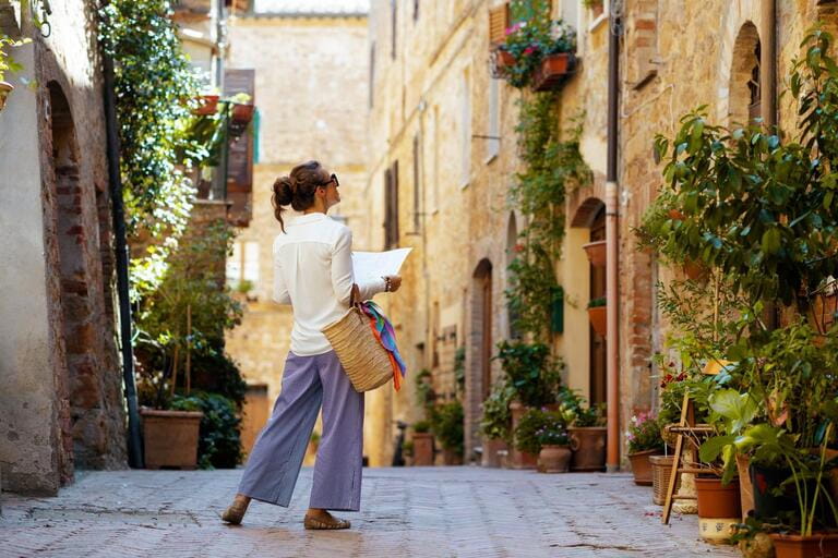 Travel in Italy. Seen from behind stylish woman with map and straw bag enjoying promenade in Tuscany, Italy.